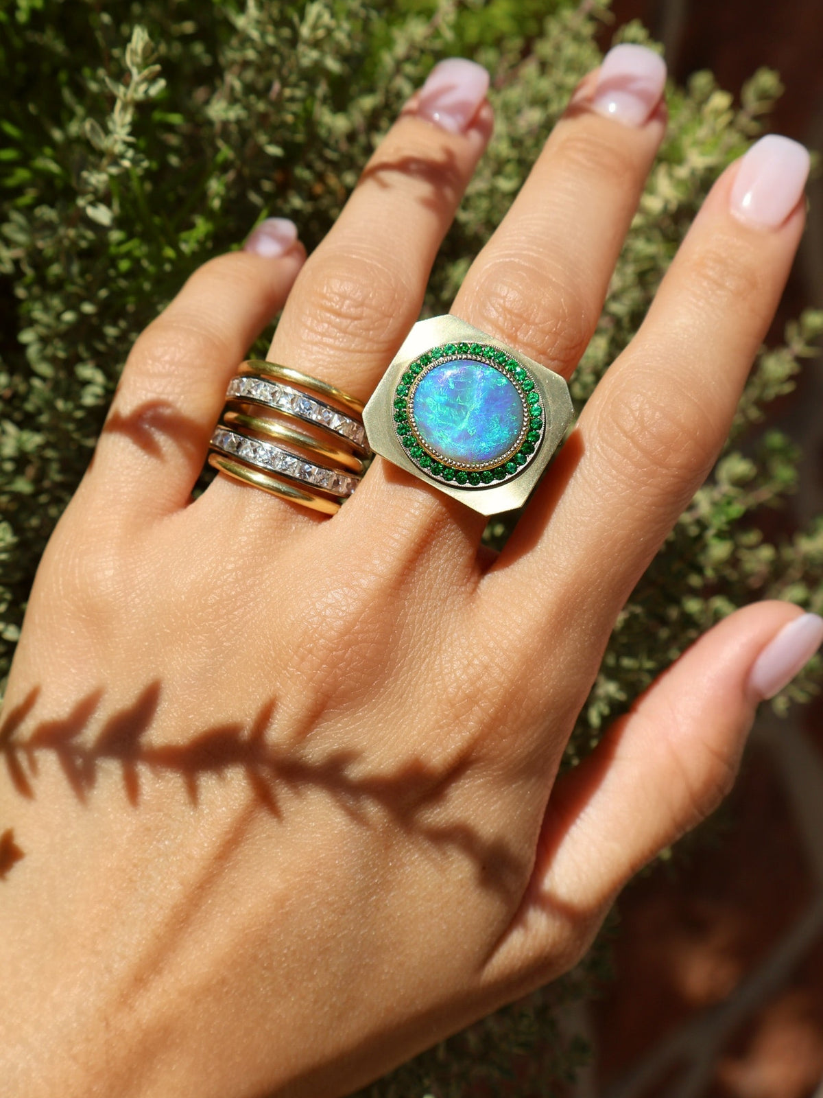 An 18k yellow gold signet-style ring featuring an oval Australian black opal surrounded by a halo of green tsavorites by Sylva & Cie