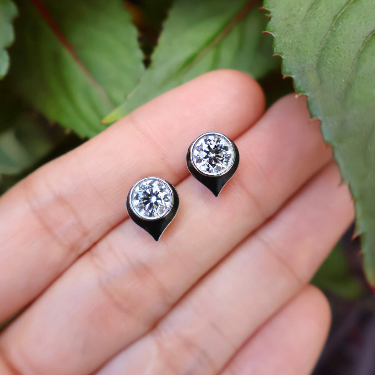 A pair of white gold stud earrings with round-cut diamond  in a teardrop-shaped setting with black enamel